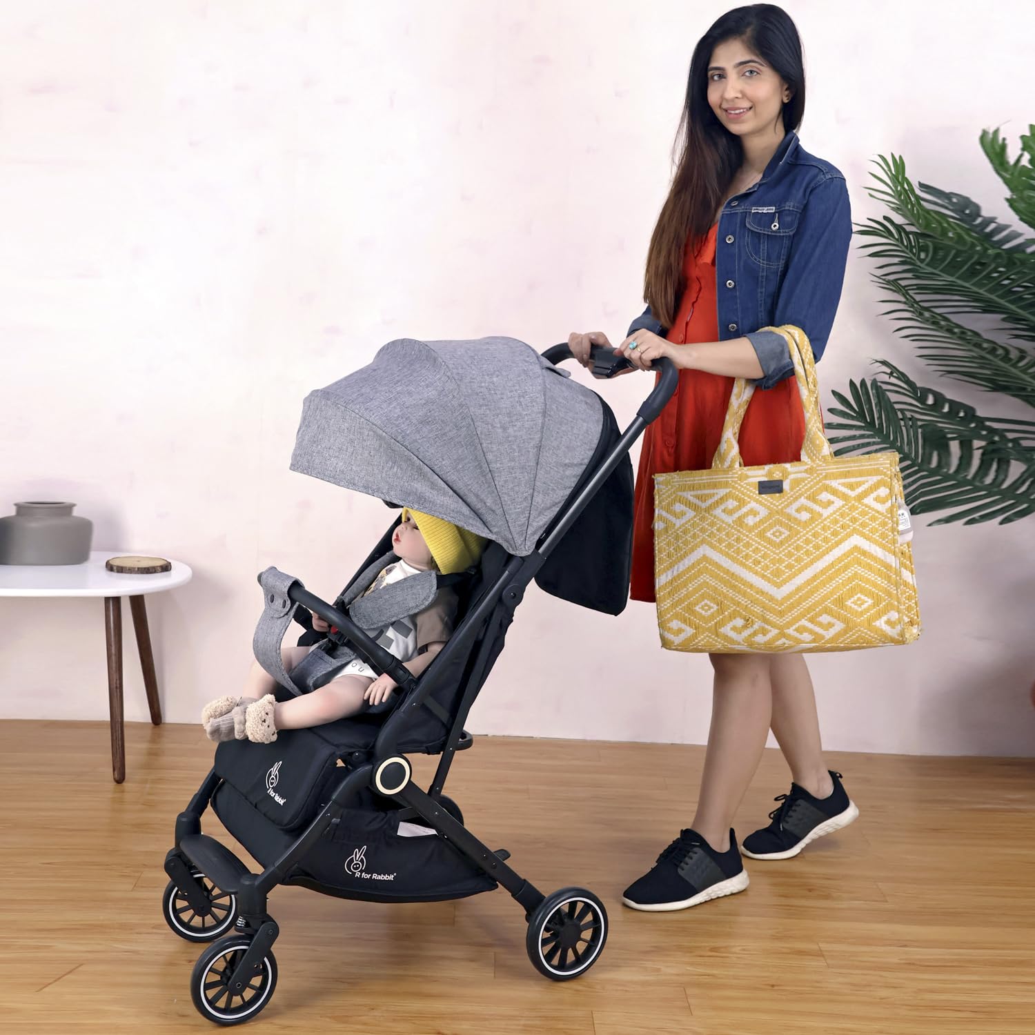 Woman pushing a stroller with a child inside, holding a yellow bag in a room setting.